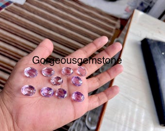 Puede incluir: Una mano sosteniendo una colección de piedras preciosas ovaladas de color púrpura claro. Las piedras preciosas son lisas y pulidas, con un ligero brillo.
