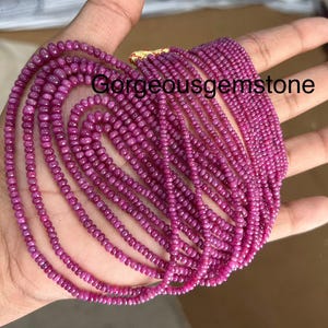 May include: A strand of pink ruby beads, approximately 2mm in diameter, strung on a thread. The beads are round and have a smooth, polished finish. The strand is approximately 18 inches long.