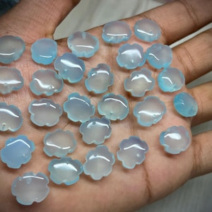 May include: A collection of cloud-shaped, translucent blue gemstones. The gemstones are held in a hand, showcasing their delicate, floral-like design. The stones have a polished, smooth surface, and vary slightly in color.