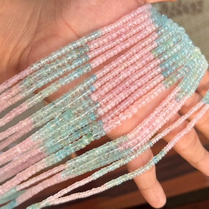 Könnte beinhalten: Stränge aus kleinen, runden Perlen in abwechselnden Abschnitten aus Rosa und Hellblau. Die Perlen sind aufgefädelt und bilden eine zarte und farbenfrohe Darstellung. Die Perlen werden in einer Hand gehalten.