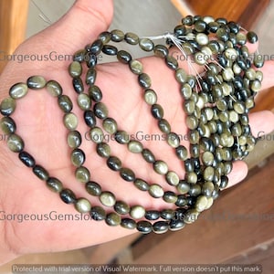 Könnte beinhalten: Nahaufnahme von Strängen oval geformter Obsidianperlen. Die Perlen haben einen goldenen Schimmer und variieren in der Farbe von dunkel bis hell. Die Edelsteine sind aufgefädelt und zeigen ihre Textur und Farbvariationen.