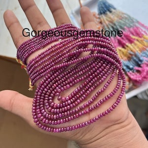 Puede incluir: Una hebra de cuentas de rubí, de aproximadamente 2 mm de diámetro, con un color rojo intenso. Las cuentas están enhebradas en un hilo transparente y están dispuestas en una pila suelta. Las cuentas son lisas y pulidas, y tienen un ligero brillo.
