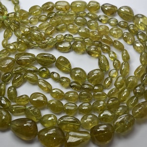 May include: A collection of olive-green gemstone beads, featuring a variety of shapes and sizes. The beads, including oval and teardrop forms, have a polished, translucent finish. They are strung together, suitable for a necklace or bracelet.