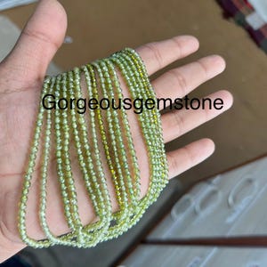 Könnte beinhalten: Eine Hand hält mehrere Stränge grüner Edelsteinperlen. Die Perlen sind rund und haben eine facettierte Oberfläche. Die Perlen sind auf einem durchsichtigen Faden aufgefädelt.