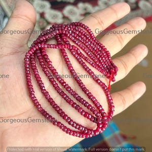 May include: Strands of faceted, deep red gemstones are held in a hand. The gemstones are strung together, forming multiple rows of beads. The image has the text "GorgeousGemstone" in the corners.
