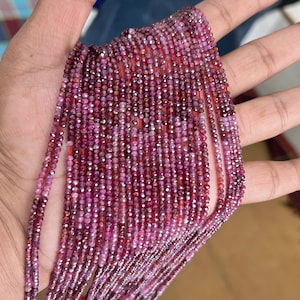 Könnte beinhalten: Eine Strähne aus rosafarbenen Rubinperlen mit facettiertem Finish, auf einem dünnen Faden aufgereiht. Die Perlen sind klein und gleichmäßig in der Größe, was einen zarten und eleganten Look erzeugt.