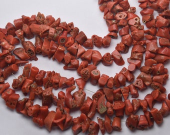 May include: A strand of coral beads, featuring a variety of shapes and sizes. The beads are a deep red color and have a natural, rough texture.