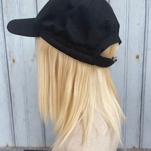 May include: A black baseball cap with a curved brim. The cap is made of a textured fabric and has a simple, classic design. The cap is shown on a mannequin head with blonde hair.