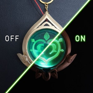 May include: A gold-colored pendant with a green, glowing heart-shaped design inside. The pendant is on a black background and the words "OFF" and "ON" are visible on either side of the pendant.