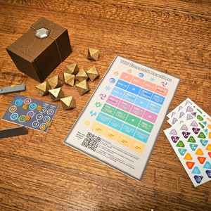 Könnte beinhalten: Ein Satz goldener Würfel mit einer braunen Box, einem grauen Lineal, einer Karte mit einem QR-Code und einer Tabelle mit dem Text "100 Elemental Resolutions" sowie vier Blättern mit Aufklebern mit verschiedenen Symbolen.