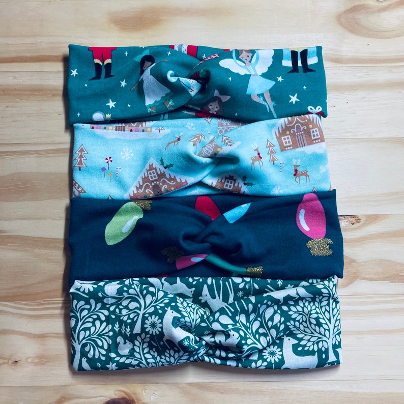 May include: Four Christmas-themed headbands with a twist knot design. The headbands are made of fabric with different patterns, including a green background with a white snowflake, a blue background with a gingerbread house, a green background with a red and white candy cane, and a green background with a white floral pattern.