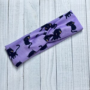 Pode incluir: Faixa de cabe&ccedil;a roxa com estampa de gato preto. A faixa de cabe&ccedil;a &eacute; feita de um tecido macio e el&aacute;stico e &eacute; perfeita para adicionar um toque de fantasia a qualquer roupa.