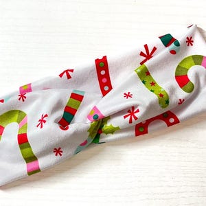 Puede incluir: Diadema blanca con estampado navideño con bastones de caramelo, copos de nieve y calcetines. La diadema está hecha de un tejido suave y elástico.