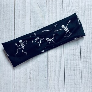 Pode incluir: Faixa de cabe&ccedil;a el&aacute;stica preta com um padr&atilde;o de esqueleto branco. A faixa de cabe&ccedil;a &eacute; torcida e tem um n&oacute; no centro.