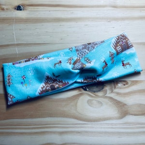 May include: A blue and brown patterned headband with a gingerbread house design. The headband is twisted and has a knot in the center.