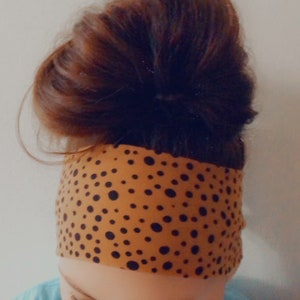 May include: A brown headband with black polka dots. The headband is worn on a person's head with their hair pulled back in a bun.