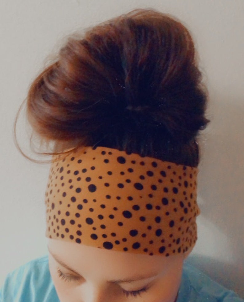 May include: A brown headband with black polka dots. The headband is worn on a person's head with their hair pulled back in a bun.