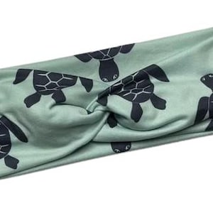 May include: A green headband with a repeating pattern of black sea turtles. The headband is twisted and has a knot in the centre.