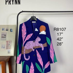 May include: A royal blue blazer featuring a hand-painted design of a lavender leopard resting on a brown branch, surrounded by pink and green tropical leaves and a sun. The text PRYNN, R8107, 17", 42", and 28" is visible on the image.