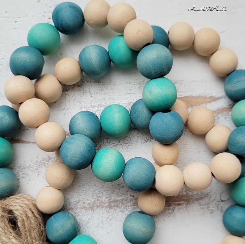 May include: A strand of wooden beads in shades of blue and green, with a natural wood colour. The beads are strung together on a twine cord.