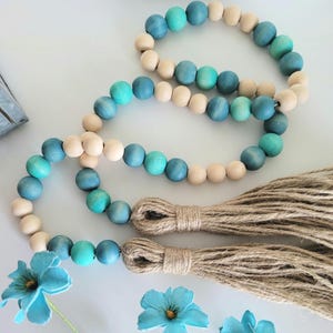 May include: A wooden bead garland with blue and natural wood beads and two brown tassels. The garland is made of round beads and is strung together with a natural twine.