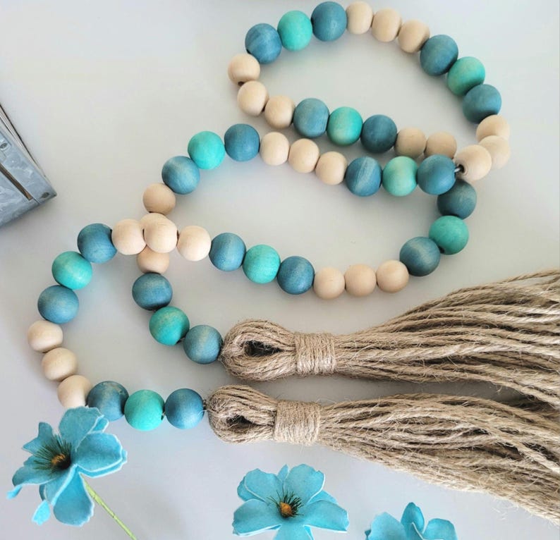 May include: A wooden bead garland with blue and natural wood beads and two brown tassels. The garland is made of round beads and is strung together with a natural twine.