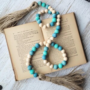 May include: A teal and white beaded garland with a jute tassel on each end. The garland is draped over an open book.