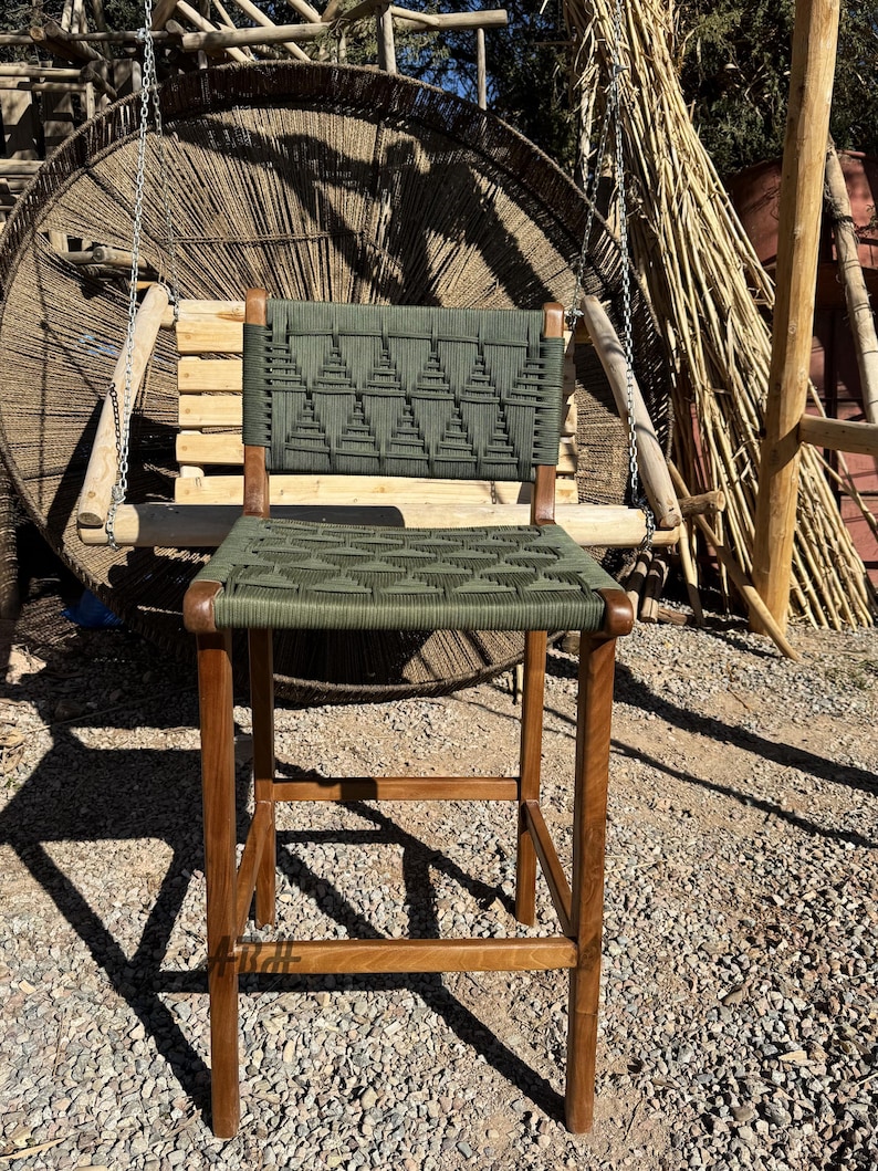 Op de afbeelding: Een houten barstoel met een groene geweven zitting en rugleuning. De zitting en rugleuning zijn geweven met een geometrisch patroon van driehoeken.