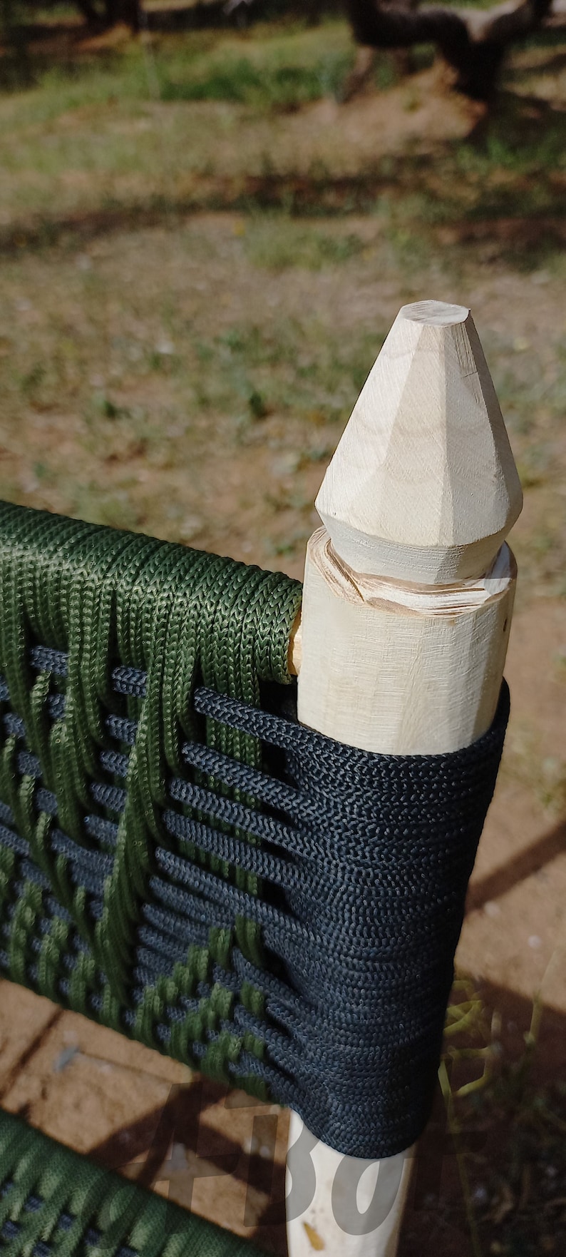 Pode incluir: Close-up de uma cadeira de madeira com um assento tecido verde e preto. A cadeira tem um topo pontiagudo &uacute;nico no poste traseiro.