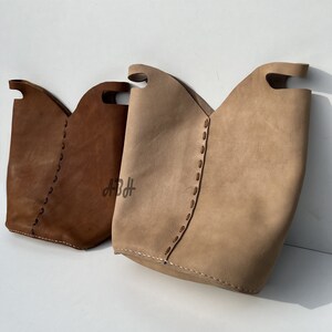 May include: Two leather tote bags with stitched detailing. One bag is brown and the other is beige.