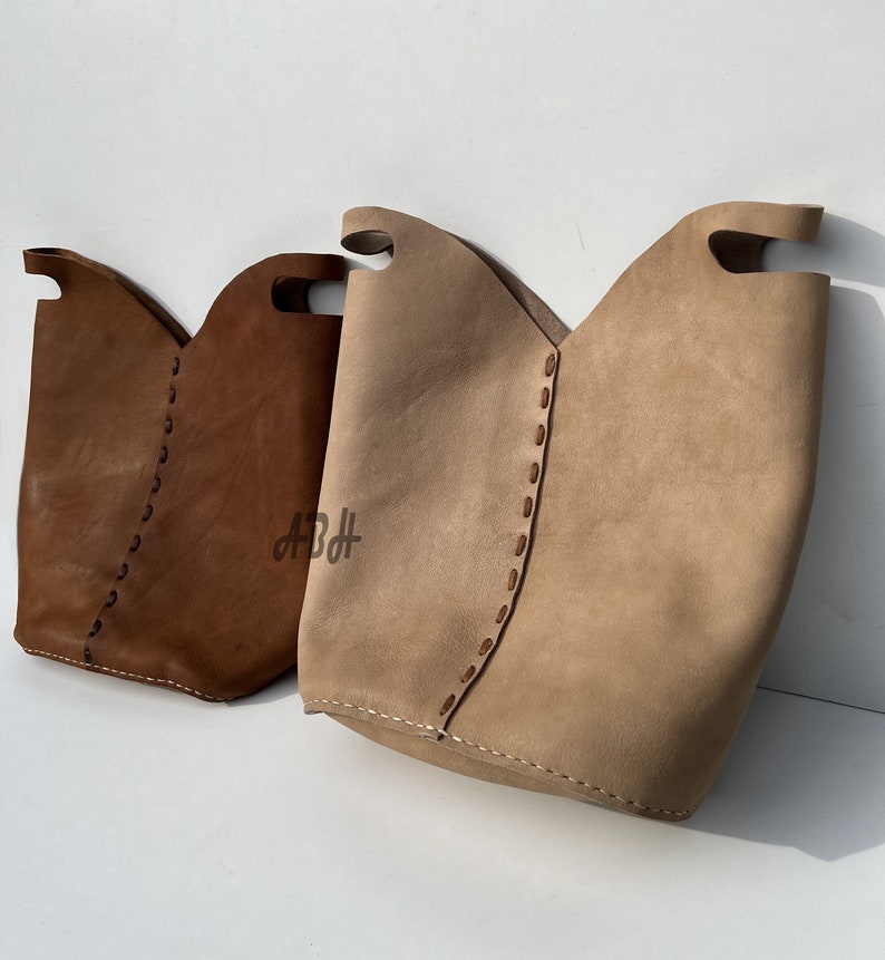 May include: Two leather tote bags with stitched detailing. One bag is brown and the other is beige.