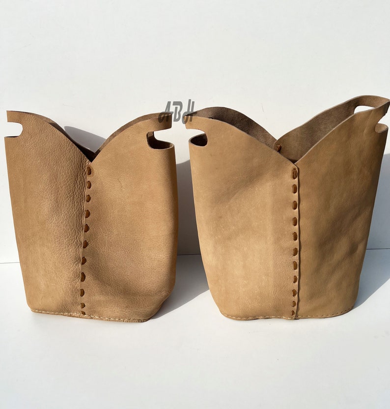 May include: Two tan leather storage baskets with stitched detailing. The baskets are empty and have a slightly distressed look.
