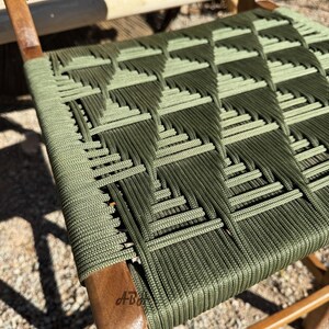 Op de afbeelding: Een groene geweven stoelzitting met een ruitpatroon. De stoel is gemaakt van hout en heeft een label met de tekst "A-B" aan de zijkant.