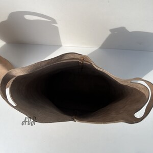 May include: A light brown leather tote bag with two handles. The bag is empty and the inside is visible.