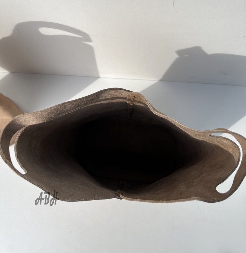 May include: A light brown leather tote bag with two handles. The bag is empty and the inside is visible.