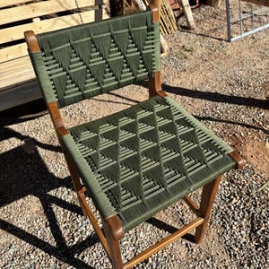 Op de afbeelding: Een houten stoel met een groene geweven zitting en rugleuning. De stoel heeft een eenvoudig ontwerp met een rechthoekige zitting en rugleuning.