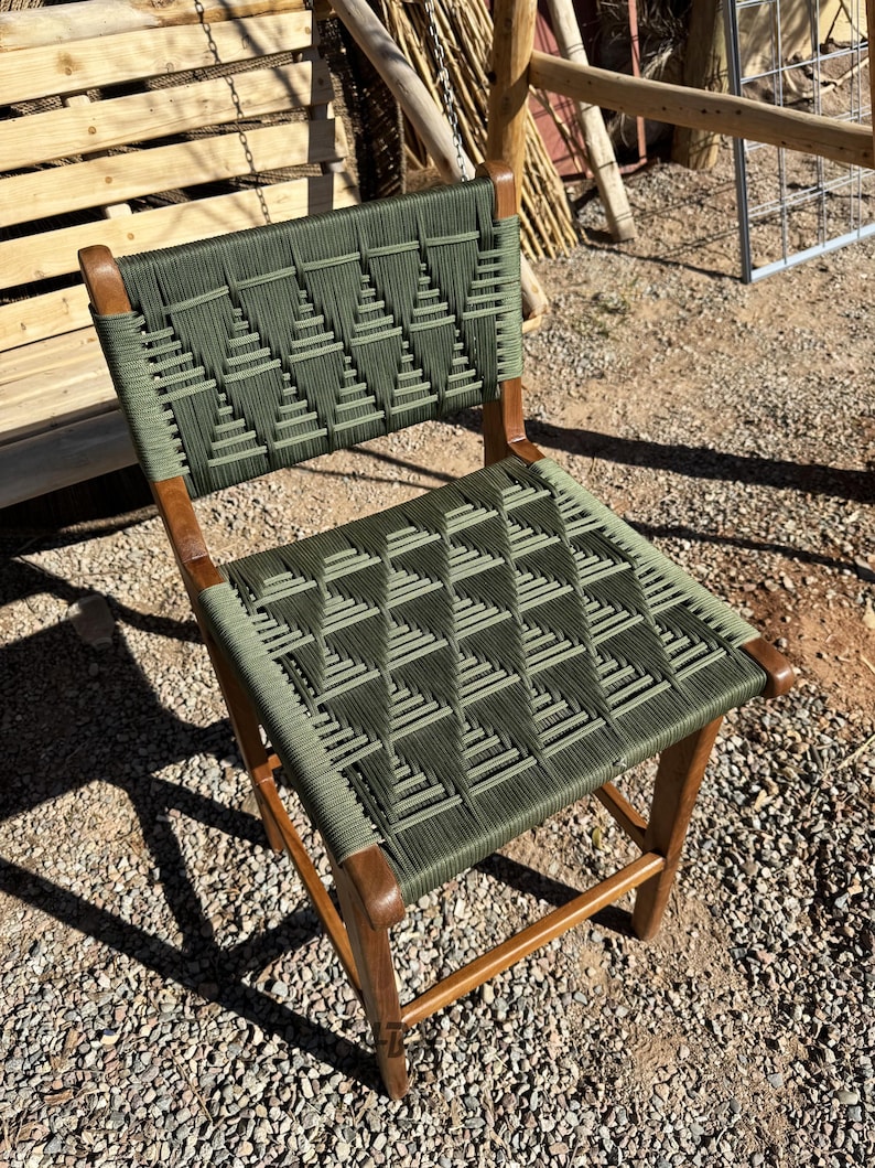 Op de afbeelding: Een houten stoel met een groene geweven zitting en rugleuning. De stoel heeft een eenvoudig ontwerp met een rechthoekige zitting en rugleuning.