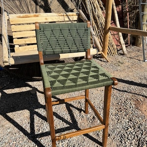 May include: A green woven bar stool with a wooden frame. The seat and back are woven with a geometric pattern.