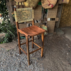 May include: A wooden bar stool with a woven back and a brown leather seat. The stool is made of dark wood and has a simple design.