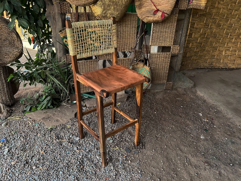 May include: A wooden bar stool with a woven back and a brown leather seat. The stool is made of dark wood and has a simple design.