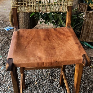 May include: A wooden chair with a woven back and a brown leather seat. The chair is sitting on a gravel surface.