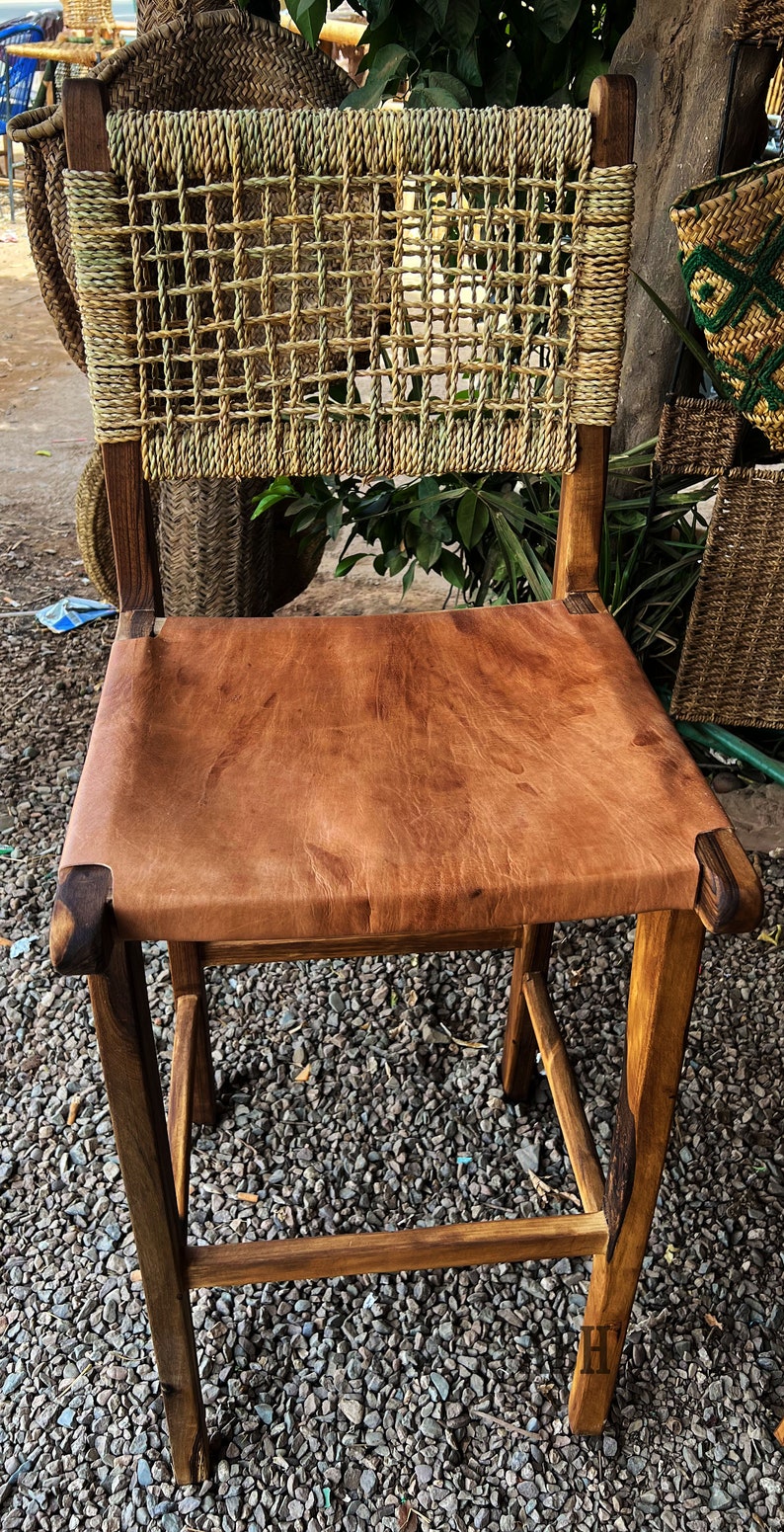 May include: A wooden chair with a woven back and a brown leather seat. The chair is sitting on a gravel surface.