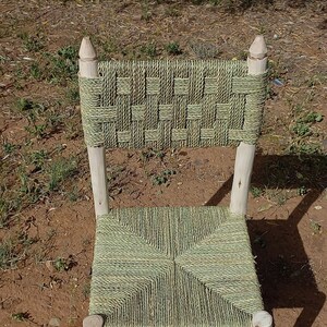 Pode incluir: Uma cadeira tecida com um assento e encosto tecidos de cor verde e natural. A cadeira &eacute; feita de madeira natural e tem um design simples.