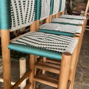 Peut inclure: Ensemble de quatre chaises en bois avec des sièges en corde tressée verte et blanche. Les chaises sont en bois naturel et ont un aspect rustique.