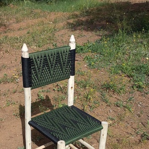 Pode incluir: Uma cadeira de madeira com assento e encosto tecidos em verde e preto. A cadeira tem um design simples com quatro pernas e um assento retangular.