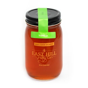 May include: A glass jar of Tupelo honey with a green label that reads "Tupelo 100% Raw Honey" and "East Hill Honey Co." The jar is 21 oz (595.3g).