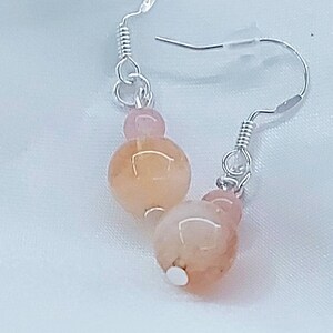 Può includere: Un paio di orecchini pendenti in argento con due perline di vetro rosa e pesca.