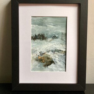 Op de afbeelding: Een ingelijst schilderij met een besneeuwd landschap en een klein bouwwerk in de verte. Het kunstwerk bevat dikke, textuurrijke penseelstreken in tinten wit, grijs en bruin, met de handtekening LH Fields in de rechterbenedenhoek.