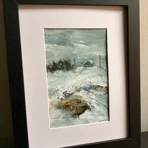 Op de afbeelding: Een ingelijst olieverfschilderij met een besneeuwd landschap en een kleine hut in de verte onder een grijze lucht. Het kunstwerk bevat dikke, textuurrijke penseelstreken in tinten wit, grijs en bruin, met de handtekening LitFields in de hoek.