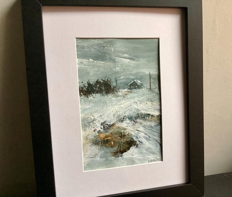Op de afbeelding: Een ingelijst olieverfschilderij met een besneeuwd landschap en een kleine hut in de verte onder een grijze lucht. Het kunstwerk bevat dikke, textuurrijke penseelstreken in tinten wit, grijs en bruin, met de handtekening LitFields in de hoek.